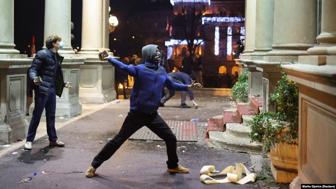 Demonstrant baca kamen na policajce koji čuvaju vrata gradske kuće tokom protesta pristalica opozicione koalicije "Srbija protiv nasilja", 24. decembra 2023. 