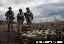 Бійці спецпідрозділу з розмінування Нацполіції стоять біля знешкоджених протитанкових мін під час операції з розмінування біля міста Ізюм, Харківська область, Україна, 24 жовтня 2023 року