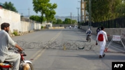 Residents return on a street partially blocked by barbed wire a day after an army cantonment was attacked by a militant suicide squad in Bannu on July 16.
