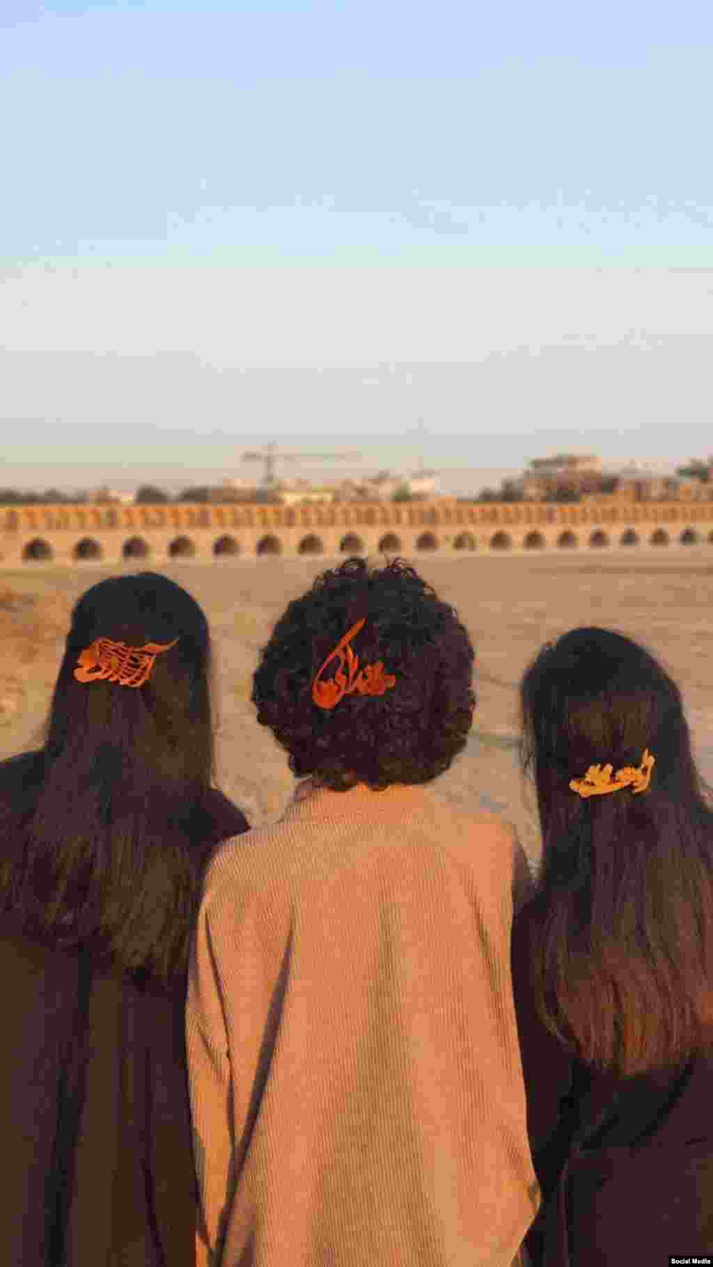 سه زن معترض اصفهانی با شعار «زن زندگی آزادی» در مقابل بستر خشک‌شده زاینده‌رود نشسته‌اند.