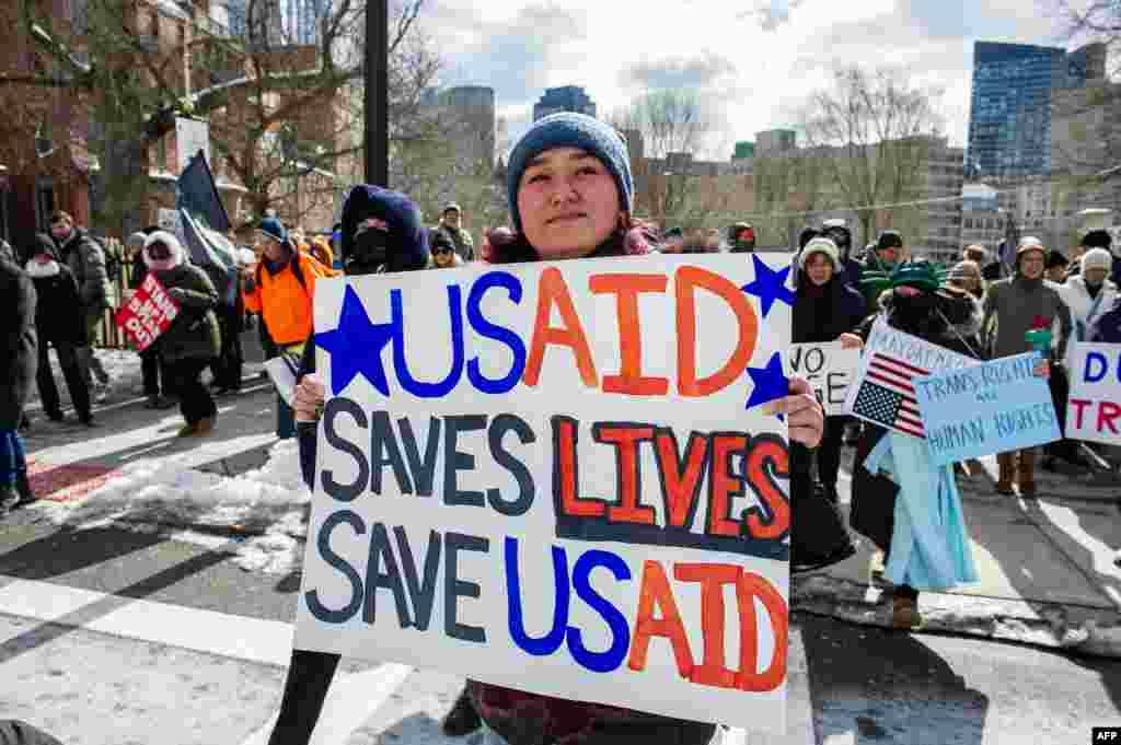 Жінка тримає плакат на підтримку USAID, позаду інші демонстранти, що мітингують проти президента США Дональда Трампа та його політики під час протесту біля будівлі Палати представників штату Массачусетс у День президентів 17 лютого 2025 року в Бостоні, штат Массачусетс, США.Адміністрація президента США Дональда Трампа повідомила Конгресу про скорочення майже всіх робочих місць у USAID і закриття агентства, яке розподіляло міжнародну допомогу Сполучених Штатів. Це зачепило й Україну