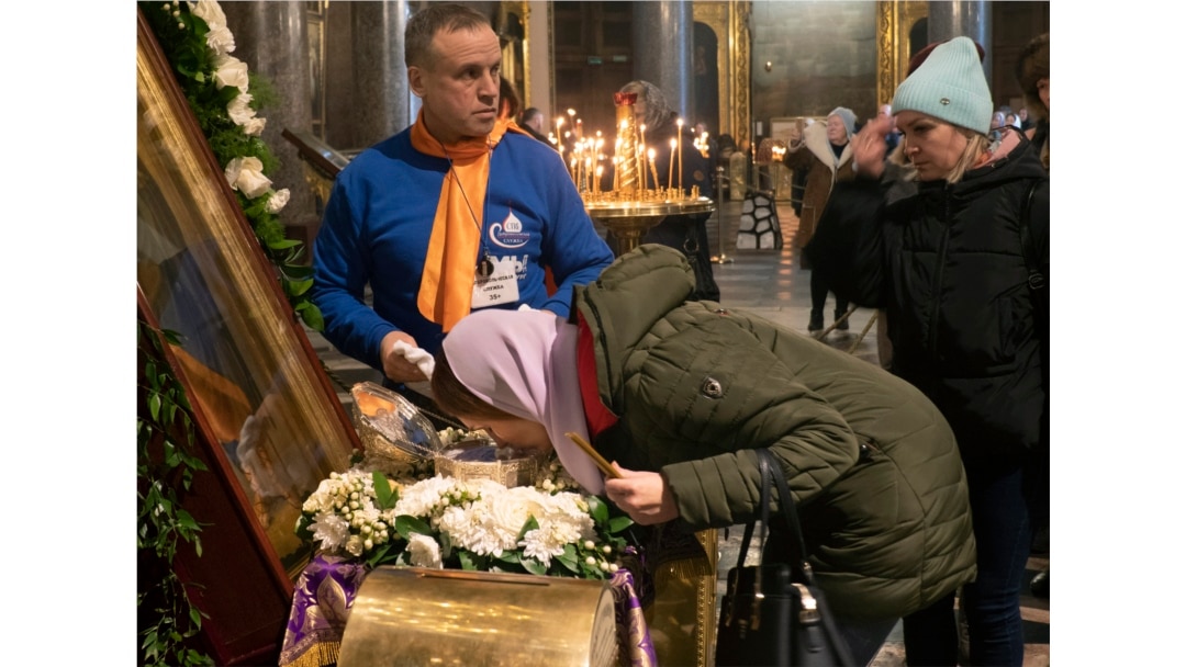 Вірянка РПЦ цілує мощі св. Івана Хрестителя, завдання волонтера – протирати скло після кожного поцілунку. Казанський собор, Санкт-Петербург, 15 березня 2020 року