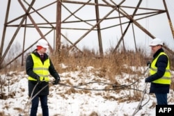 Міністр енергетики Латвії Каспарс Мелніс та керівник латвійського оператора електромереж AST Роландс Іркліс тримають в руках перерізаний дріт, який сполучав балтійську мережу з російською