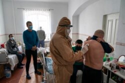 Лікар, одягнений у спеціальний костюм для захисту від коронавірусу, перевіряє пацієнта на коронавірус стетоскопом під час вечірнього огляду в лікарні в Почаєві, 1 травня 2020 року