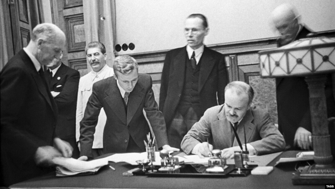 Міністр закордонних справ СРСР В'ячеслав Молотов (праворуч, сидить) підписує пакт Молотова-Ріббентропа. Третій ліворуч – генеральний секретар ЦК ВКП(б) Йосип Сталін. Москва, 23 серпня 1939 року 